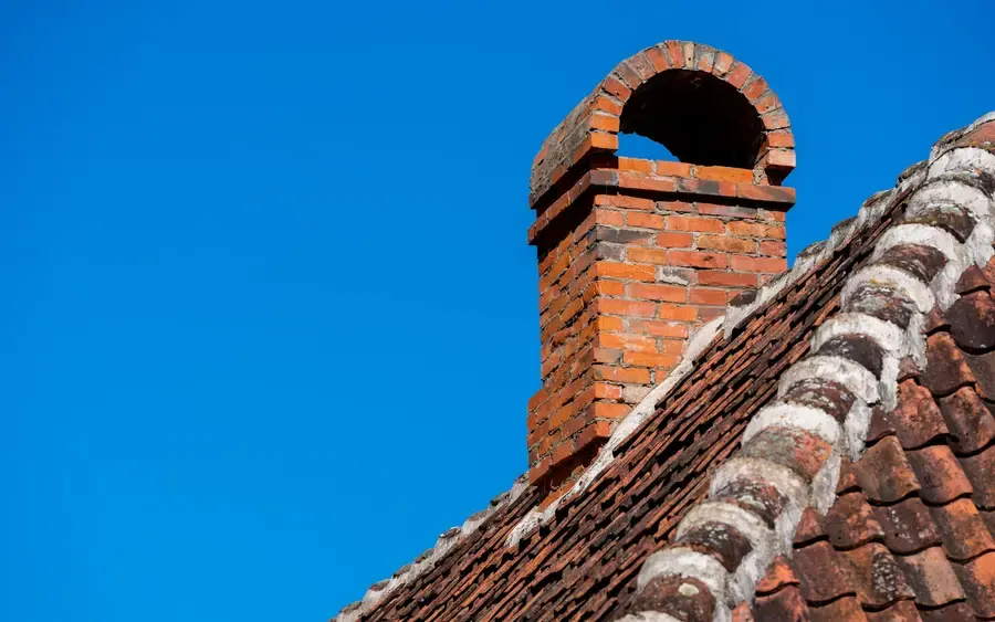 After: a rebuilt brick chimney with fresh leadwork against a blue sky