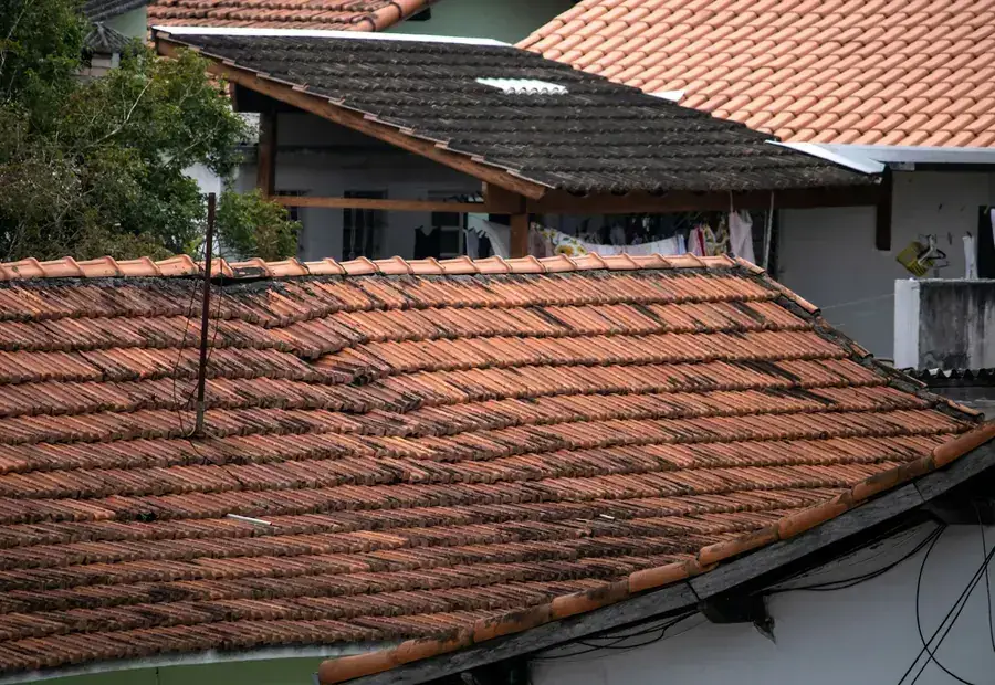 A weathered tiled roof being repaired, with slipped and worn tiles visible